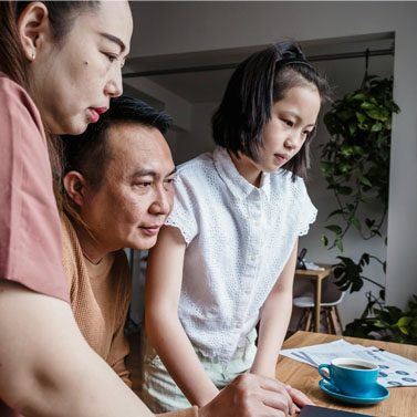 Family of three sitting at a desk and looking at a laptop together