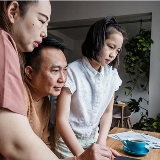 Family of three sitting at a desk and looking at a laptop together.