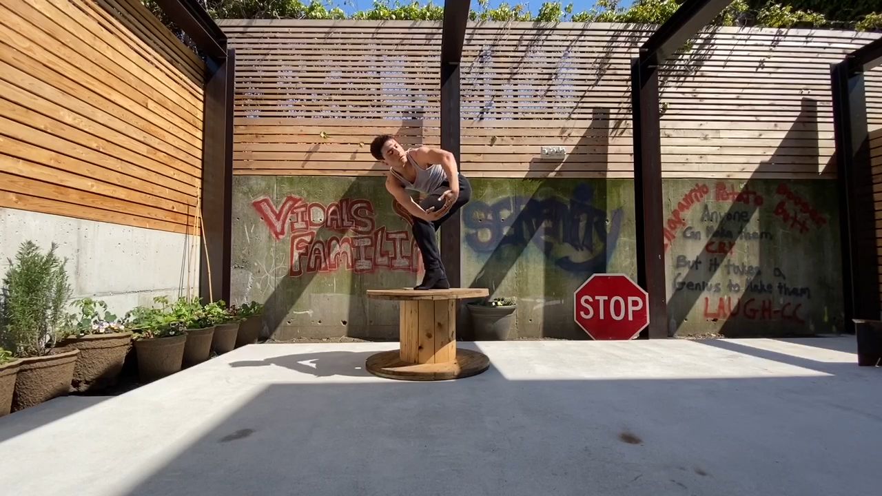 Male dancer performing in an open outdoor space standing on a large  wooden spool