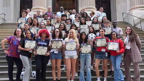 Group of high school students standing on a staircase and holding up certificates that read, 'PSAL Student Ambassadors'