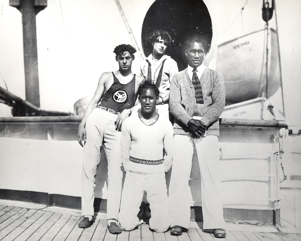 Four people, Johnny Weissmuller (left); Aileen Riggin (center, back); Duke Kahanamoku (right); and David Kahanamoku (kneeling); en route to the 1924 Paris Olympics.