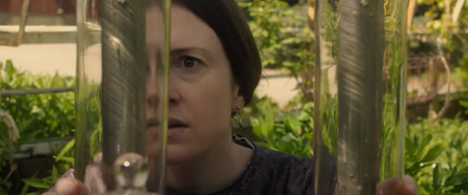 Screenshot of the short film Eunice (2018) depicting a woman with brown hair in a greenhouse inspecting glass cylinders.