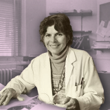 Black and white photograph of Helen Rodríguez-Trías in a lab coat at a desk.