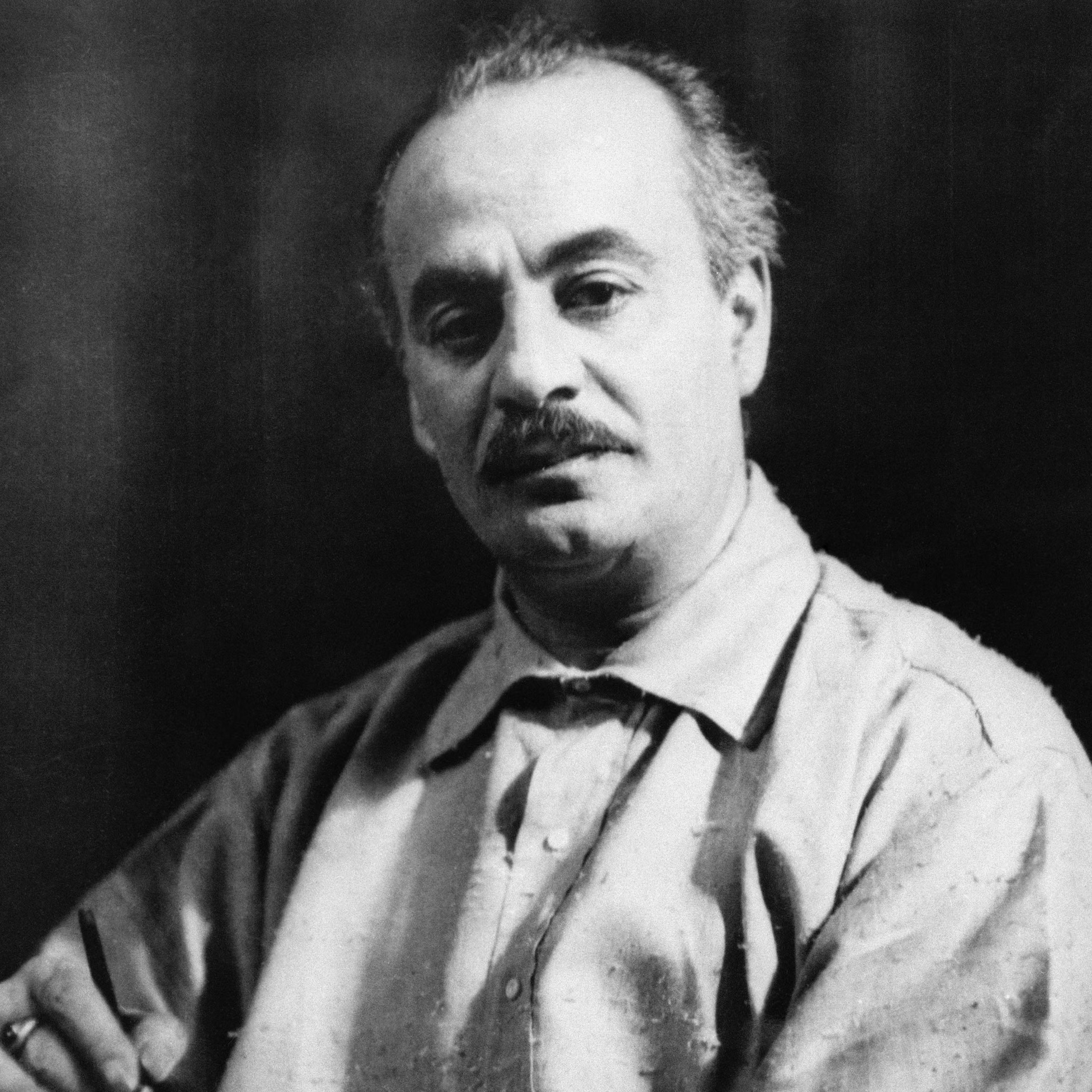 Black and white photograph of Kahlil Gibran looking at the camera with a black background.