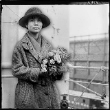Black and white photograph of Mabel Ping Hua Lee in a coat and hat holding a bouquet of flowers.