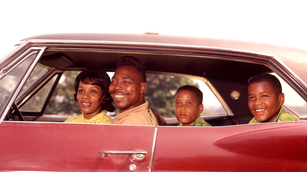 Family of Four Inside Automobile A family of four sitting inside of a 1950s-era vehicle and smiling