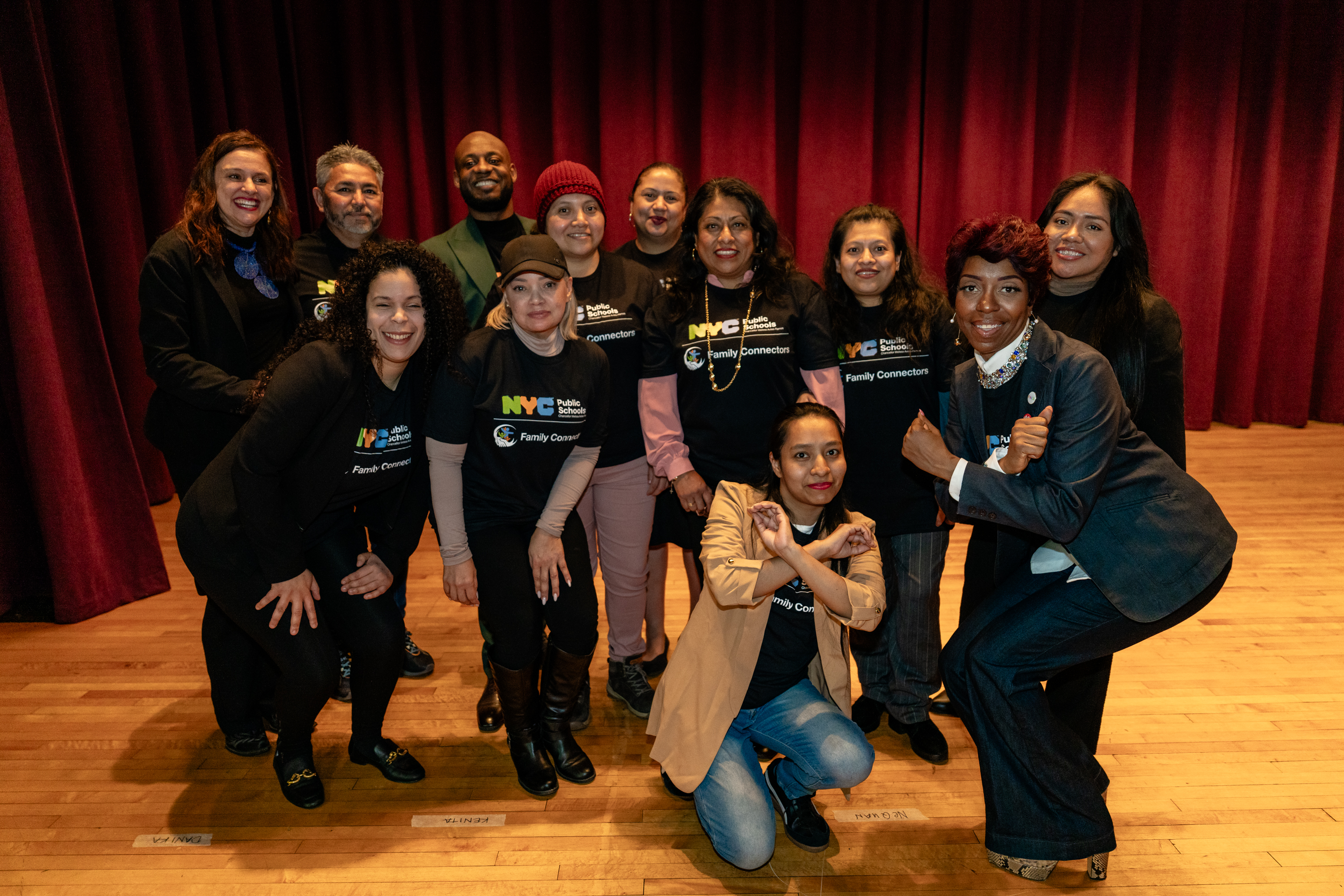 Twelve Family Connectors pose on a stage for a photo from an NYCPS Cares event.