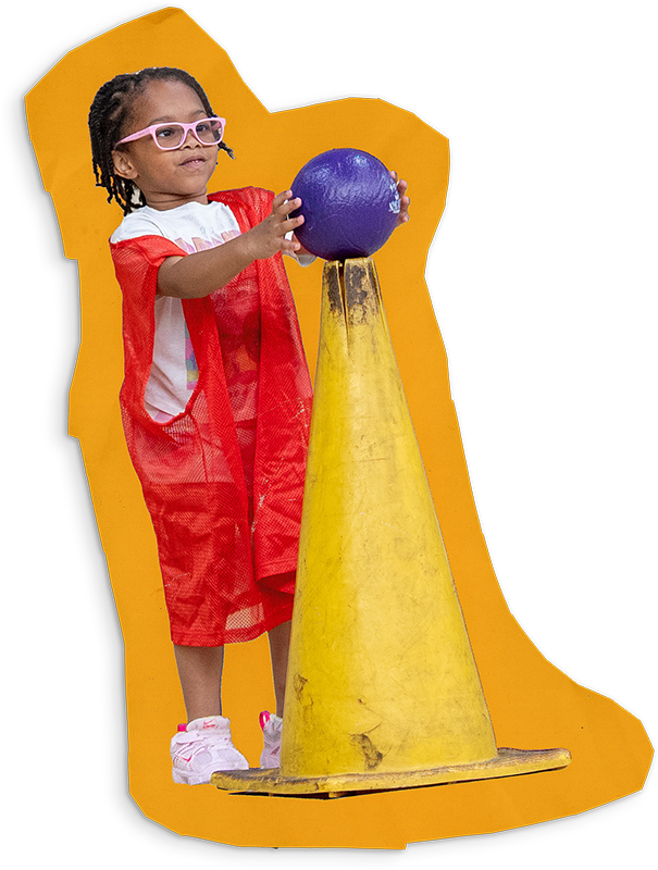 A young child balances a ball on the top of a tall traffic cone