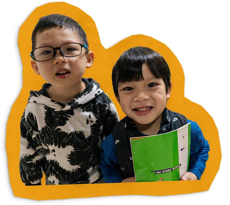 Two young children smiling while one of them holds a well-worn book