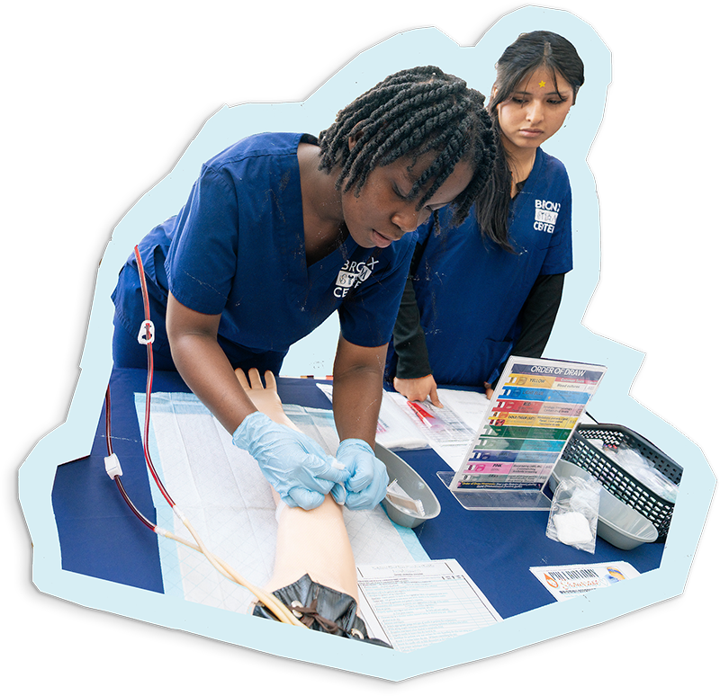 Two students dressed in medical scrubs demonstrate on practice equipment
