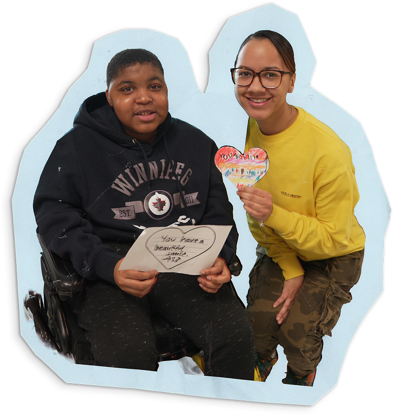 A student is holding a drawing of a heart next to a teacher holding a heart-shaped craft project