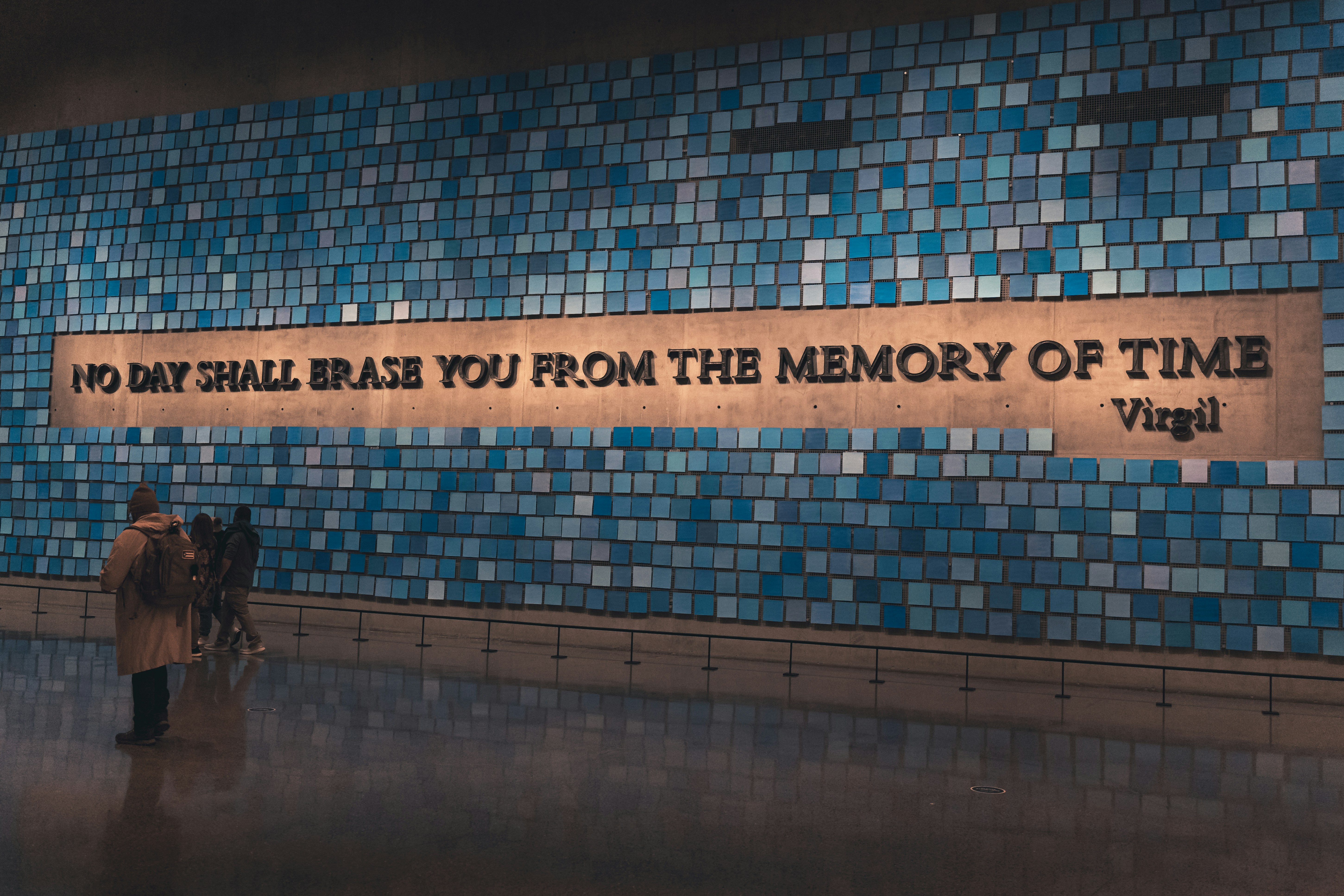 Blue tiled wall with the quote 'No day shall erase you from the memory of time' by Virgil on the wall.