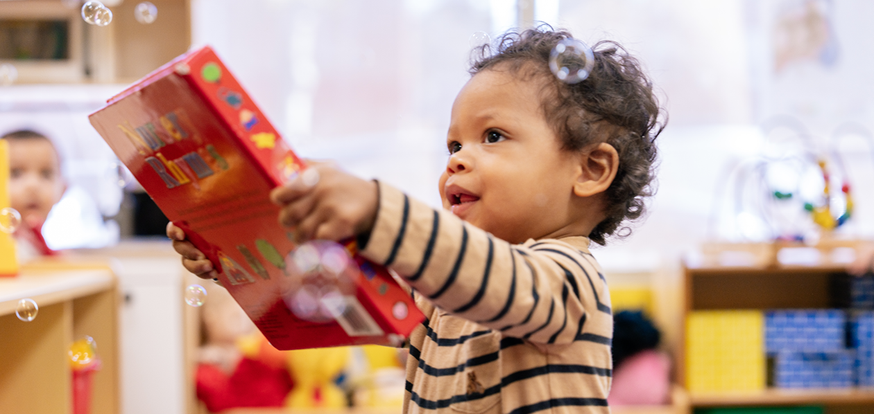A young child holds a book and looks at bubbles