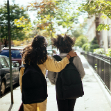 Back view of two school-aged girls with bookbags walking down a city street.
