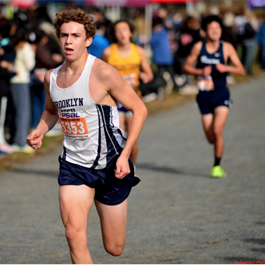 Close-up of a Brooklyn Tech cross-country student in mid-race ahead of two other student competitors in the background