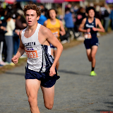 Close-up of a Brooklyn Tech cross-country student in mid-race ahead of two other student competitors in the background