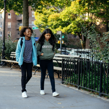 Two girls with backpacks walking on a New York City sidewalk.