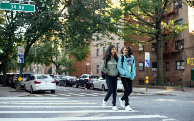 Two girls with backpacks walking on a New York City crosswalk.