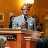 Chancellor Banks standing at a podium and holding a microphone.