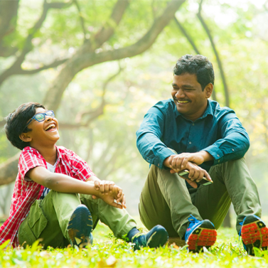 Elementary/middle school-aged child sitting on grass in a park next to an older man, and they are both laughing