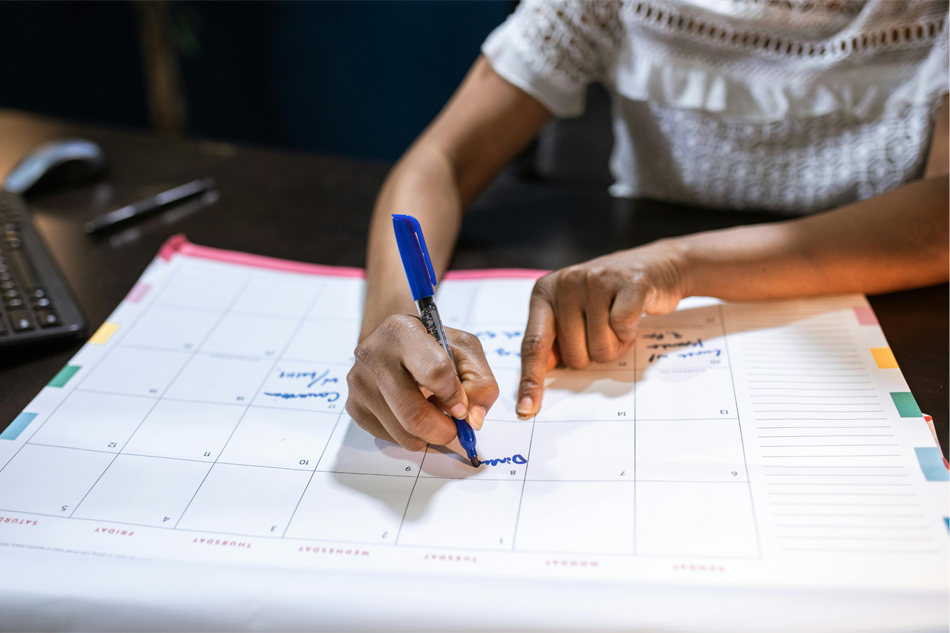 Close-up of a person writing in a desktop calendar with a blue marker.