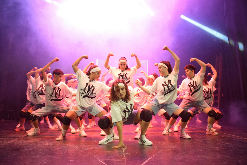 Group of dancers posing on a stage following a routine; they are all wearing shirts with the NY Yankees logo.