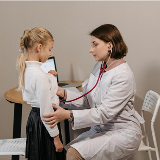 A medical professional (right) using a stethoscope to check a child (left).