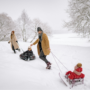 Family of four, with two adults pulling two children sitting on inner tubes in the snow.