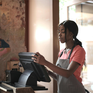 Teenaged girl standing in front of a cashier POS, ready to operate it.