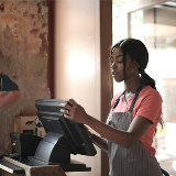 Teenaged girl standing in front of a cashier POS, ready to operate it.