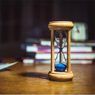 Closeup of a wooden hourglass whose sand has almost completely shifted towards the bottom of the hourglass.