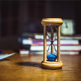 Closeup of a wooden hourglass whose sand has almost completely shifted towards the bottom of the hourglass.