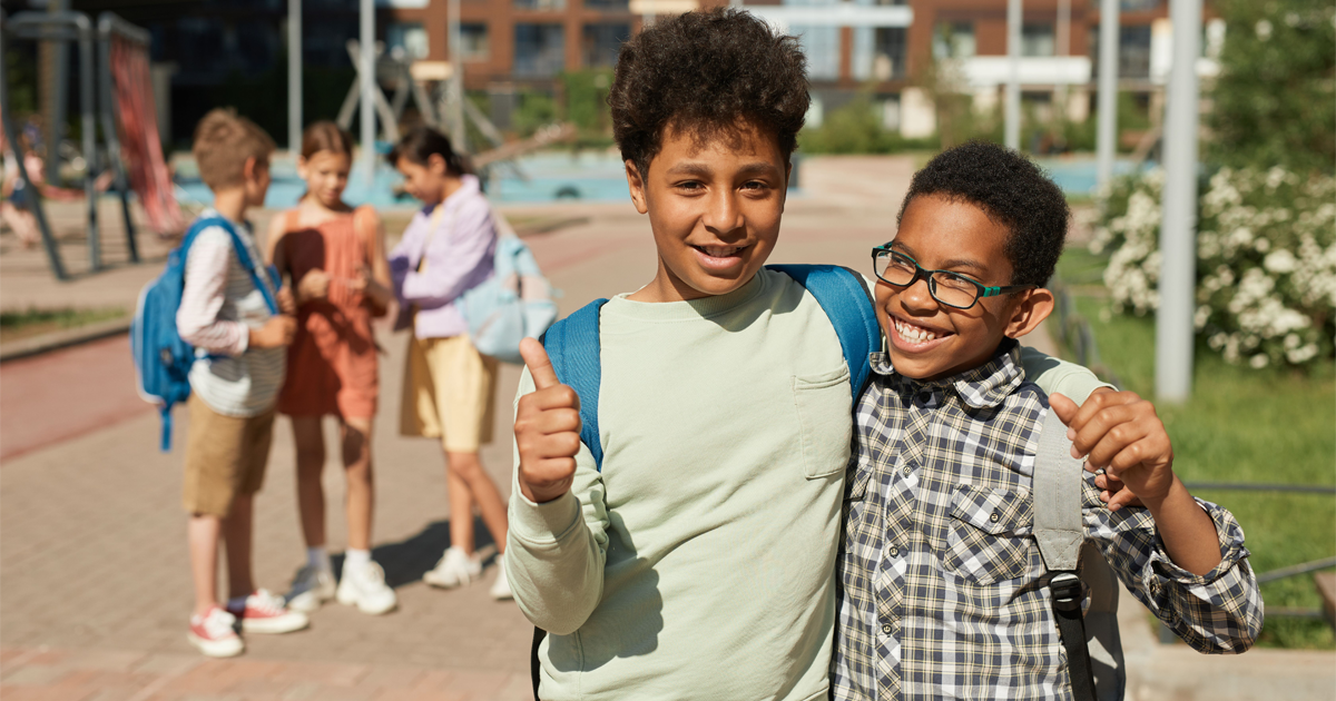 Two middle school-aged kids embracing one another outside of school.