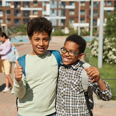 Two middle school-aged students embracing one another while walking together outside of school.