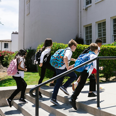 Side view of five middle school-aged children running up a set of stairs that lead into a school