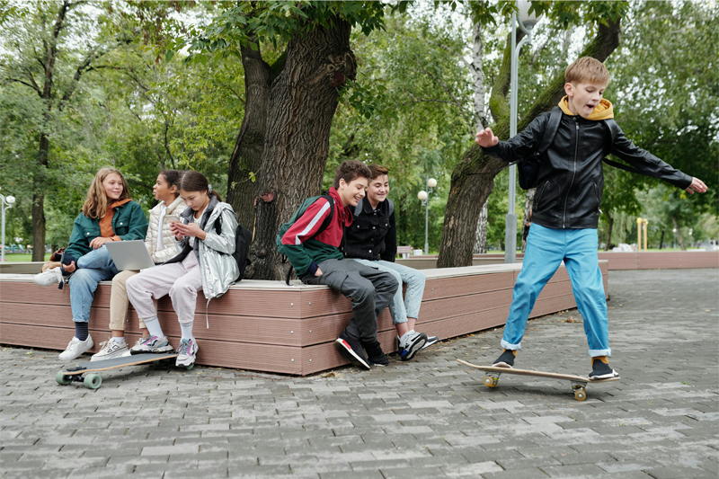 A boy skateboarding (right) while two other boys look on (middle) while three girls (left) talk to one another and paying the skateboarder no mind.