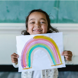 Young girl holding up a watercolor painting of a rainbow.