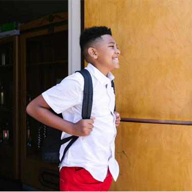 Middle school-aged boy standing at an entrance to a school and smiling.