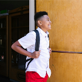 Middle school-aged boy standing at an entrance to a school and smiling.