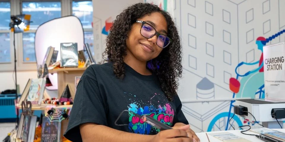 Close-up of young woman with glasses sitting at a desk with a pen in hand.