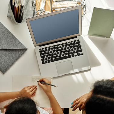 Overhead shot of a parent helping their child at a desk with a laptop on it.