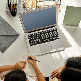 Overhead shot of a parent helping their child at a desk with a laptop on it.