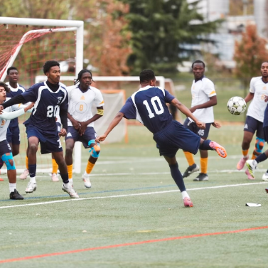 Group of boys playing soccer. The boy at the center wearing jersey number 10 is about to kick the ball, which is midair.