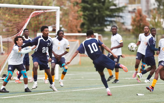 Group of boys playing soccer. The boy at the center wearing jersey number 10 is about to kick the ball, which is midair.