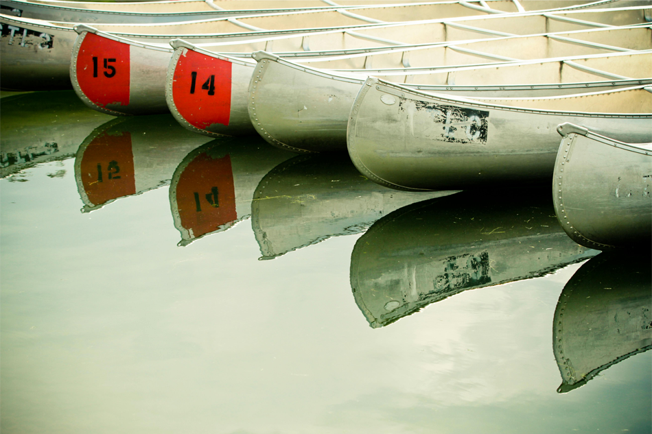 View of a row of canoes and their reflections near the shoreline of a lake