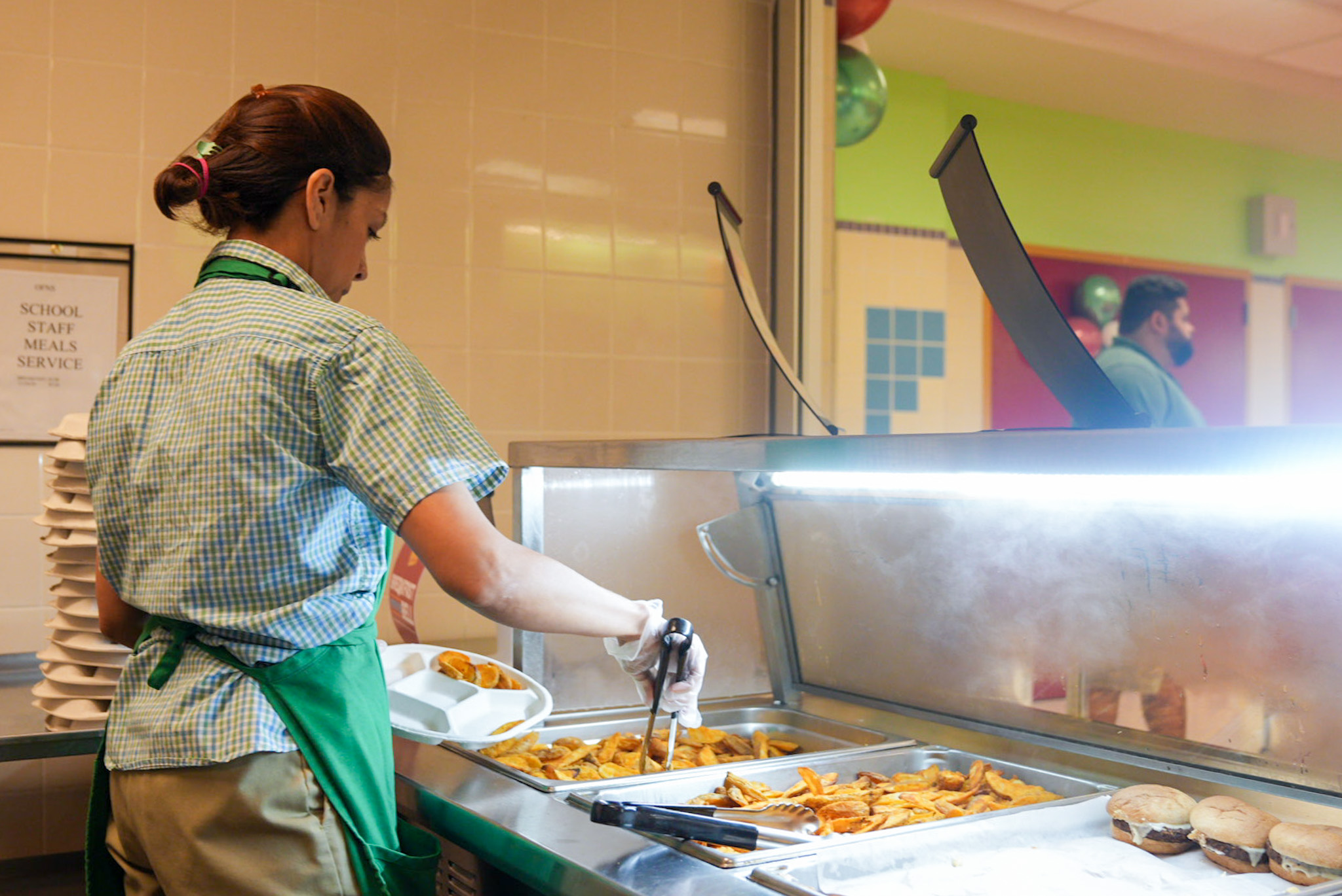 School cafeteria worker wearing a green apron assembling a plate of food.