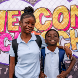 Sister and brother standing next to each other in front of a mural that reads, "Welcome Back to School"