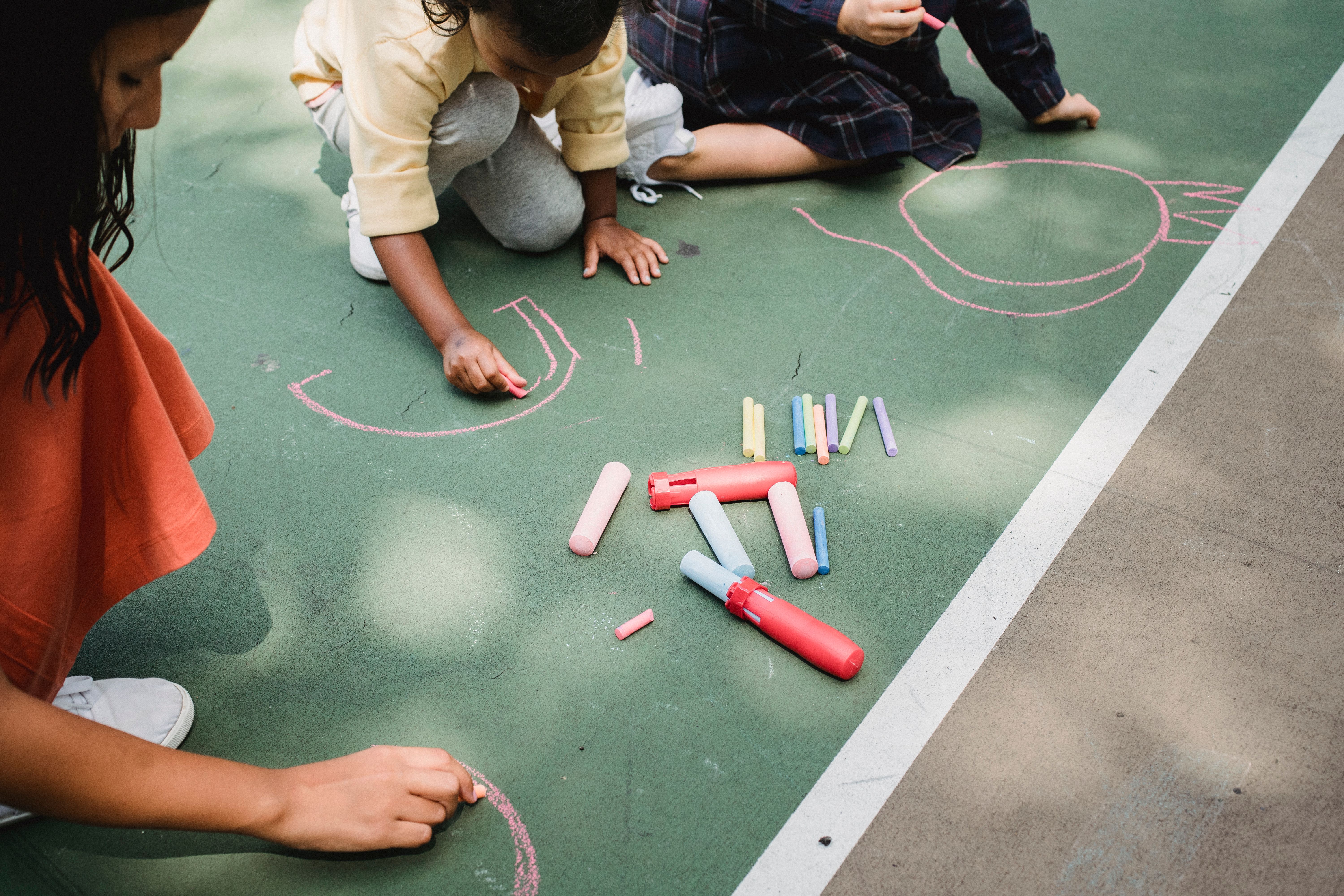 Young students and teachers make art with chalk in the school yard