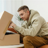 Close-up, side view of a teenager opening up a cardboard box and looking at the contents inside with a slight smile on their face.