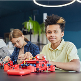 Three students sitting at a table together in a row, working on putting together robotics-related parts